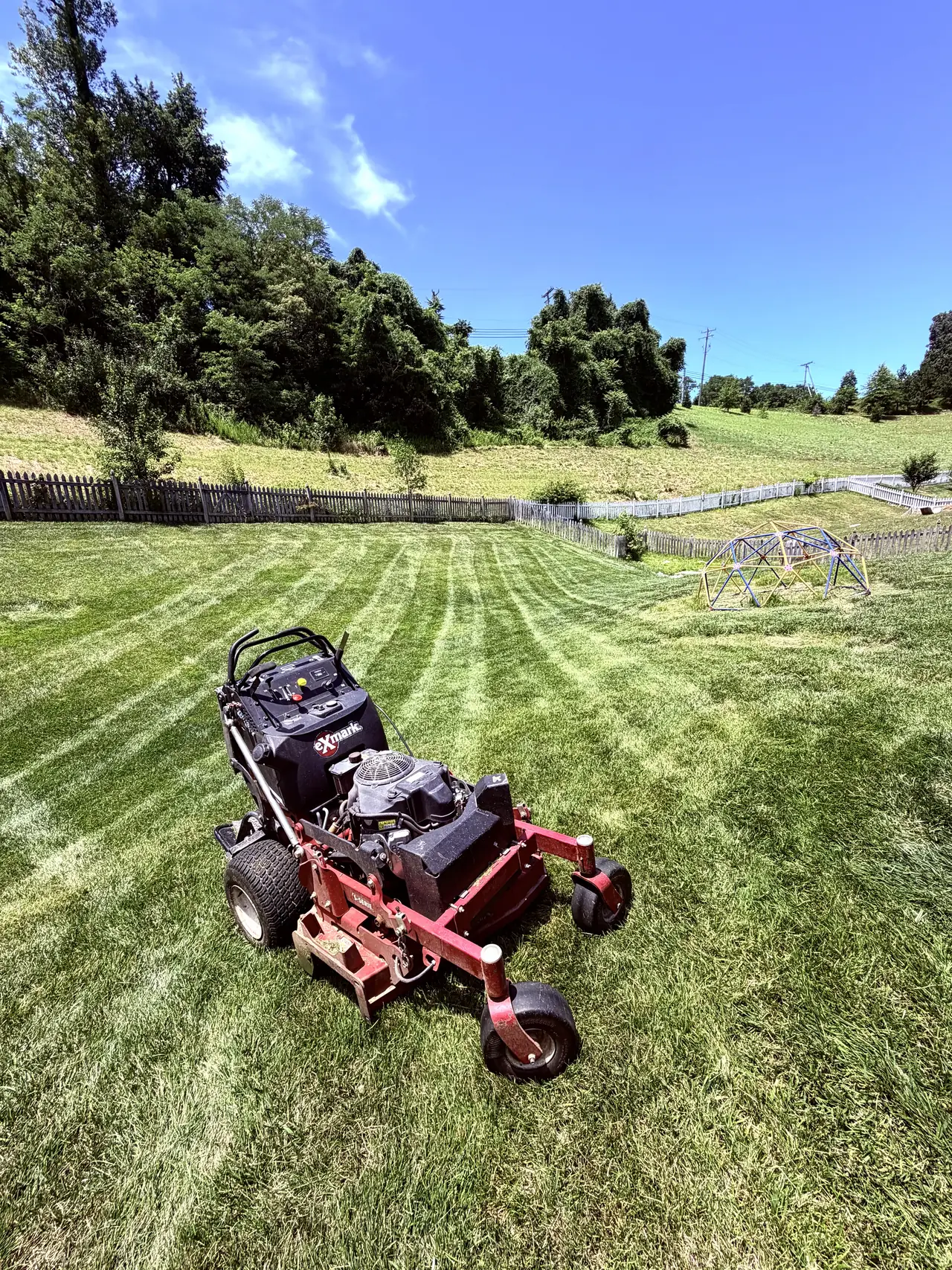 A red mower on a freshly striped lawn sloping toward a wooden fence
